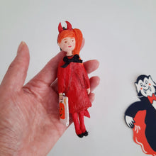 Cargar imagen en el visor de la galería, A hand holding a spun cotton girl dressed up as a devil with horns and a tail, against a white background. A vintage '80s vampire decoration sits in the background.