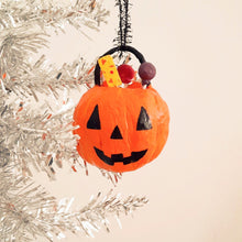 Load image into Gallery viewer, A spun cotton jack-o'-lantern bucket filled with sweets hanging from a silver tinsel tree against a plain background.