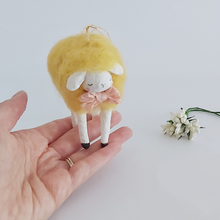 Load image into Gallery viewer, A yellow, vintage style needle felted spun cotton sheep standing on a hand. White flowers sit nearby, against a white background. Pic 2 of 7.
