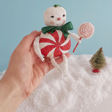 Load image into Gallery viewer, A hand holding a vintage style spun cotton Christmas candy man ornament above fake snow. A mini bottle brush tree sits below. Pic 2 of 8.