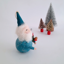 Load image into Gallery viewer, Side view of a gnome with a blue hat and outfit, holding a robin, with miniature trees in the background on a white surface.