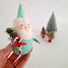 Load image into Gallery viewer, Hand holding a mint green, spun cotton Christmas gnome, surrounded by miniature bottle brush trees on a light background.