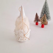 Load image into Gallery viewer, The back view of a white spun cotton gnome on a background with small, bottle brush Christmas trees in the distance.