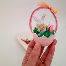 Load image into Gallery viewer, A hand holding a small decorative Easter egg with a spun cotton bunny, eggs, and chocolate bunny box inside, against a plain background.