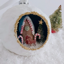 Load image into Gallery viewer, A close-up of a vintage style, spun cotton gingerbread house diorama ornament sitting on fake snow next to a mini bottle brush tree. Pic 3 of 6.