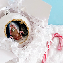 Load image into Gallery viewer, A vintage style spun cotton gingerbread house diorama ornament in a white gift box with white tissue shredding. A candy cane lays next to the box. Pic 5 of 6.