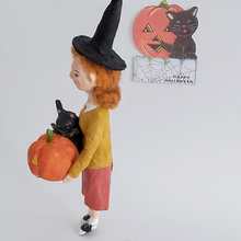 Load image into Gallery viewer, A side view of a vintage style, spun cotton Halloween girl art doll. A vintage style Halloween greeting hangs in the background. Pic 6 of 7.