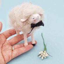 Load image into Gallery viewer, A white spun cotton needle felted sheep ornament, held in hand against a light blue background. White flowers sit next to the sheep. Pic 1 of 6.