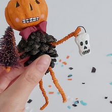 Load image into Gallery viewer, A closer view of the spun cotton skull held by the spun cotton pinecone man, against a white background. Pic 5 of 8.