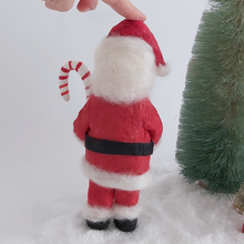 Load image into Gallery viewer, A back view of a vintage style spun cotton Santa art doll. He's standing next to a bottle brush tree on fake snow. Pic 8 of 9.