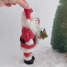Load image into Gallery viewer, A side view of a vintage style Santa art doll, standing next to a bottle brush tree. Pic 7 of 9.