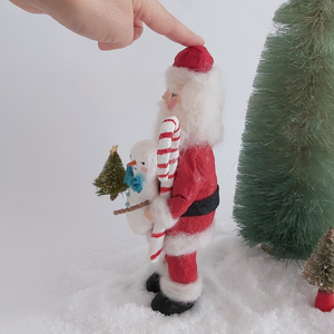 An opposite side view of a vintage style spun cotton Santa art doll, standing next to  bottle brush trees.  Pic 9 of 9. 