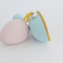 Load image into Gallery viewer, A side view of a vintage style spun cotton sheep diorama egg ornament. It's laying against pink and light blue egg ornaments. Pic 5 of 6.