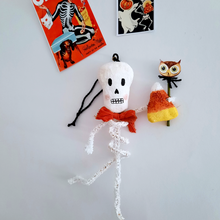 Load image into Gallery viewer, A vintage style, spun cotton pipe cleaner skeleton laying next to vintage skeleton Halloween illustrations. Pic 5 of 5.