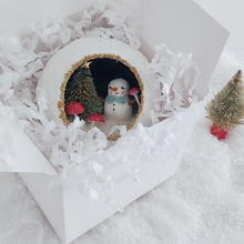 Load image into Gallery viewer, A vintage style spun cotton snowman diorama ornament, laying in a white gift box next to a mini bottle brush tree. Pic 5 of 6.