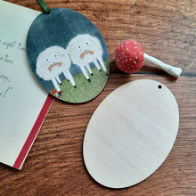 Cargar imagen en el visor de la galería, A wooden sheep ornament laying on a dark wood background, next to the blank back of another wood ornament. A vintage card and red spun cotton mushroom lay next to both.
