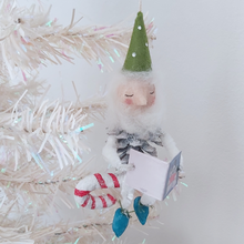 Load image into Gallery viewer, Another view of the spun cotton pine cone elf sitting on a candy cane, hanging on a white Christmas tree. Pic 3 of 10.