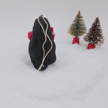 Load image into Gallery viewer, Back view of spun cotton pine cone penguin sitting on fake snow with two bottle brush trees in the distance. Pic 9 of 10. 
