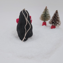 Load image into Gallery viewer, Back view of spun cotton pine cone penguin sitting on fake snow with two bottle brush trees in the distance. Pic 9 of 10.