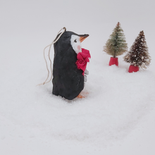 Load image into Gallery viewer, Side view of spun cotton pine cone penguin sitting on fake snow with two bottle brush trees in the distance. Pic 8 of 10.