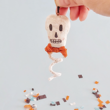 Cargar imagen en el visor de la galería, A vintage style spun cotton skeleton ornament held by hand above Halloween confetti against a light blue background. Pic 1 of 6.