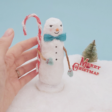 Cargar imagen en el visor de la galería, Image of a hand next to a vintage style spun cotton skinny snowman. He stands on snow against a light blue background. Pic 2 of 6.