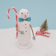 Cargar imagen en el visor de la galería, Image of a vintage style spun cotton skinny snowman holding a candy cane and standing on snow. He's against a light blue background with a vintage bottle brush tree and Merry Christmas sign behind him. Pic 3 of 6.