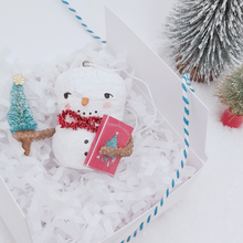 Load image into Gallery viewer, Vintage style spun cotton snowman ornament laying in white gift box with white shredding, next to bottle brush trees on a white background. Pic  5 of 8.