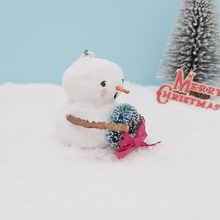 Load image into Gallery viewer, Side view of spun cotton snowman, sitting on snow against a light blue background with a bottle brush tree in the distance. Pic  6 of 8.