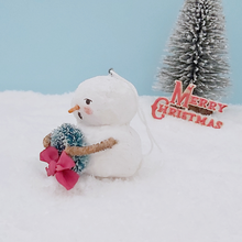 Load image into Gallery viewer, Opposite side view of vintage style spun cotton snowman. He's against a light blue background, sitting on snow, with a bottle brush tree in the distance. Pic  7 of 8.