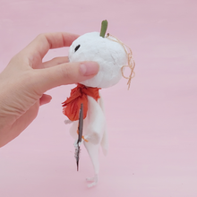 Load image into Gallery viewer, Side view of spun cotton white jack-o-lantern ghost ornament, held in hand against pink background. Pic 6 of 7.