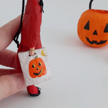 Load image into Gallery viewer, A hand holds a spun cotton devil girl ornament, with the focus on the Halloween bag she is holding. A spun cotton jack-o'-lantern is blurred in the background on a white surface.
