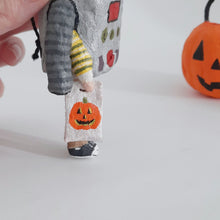 Load image into Gallery viewer, A close-up of a hand holding a small spun cotton robot ornament holding a white pumpkin bag. A larger orange jack-o'-lantern decoration is blurred in the background on a white surface.
