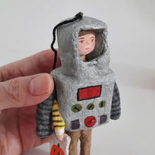 Load image into Gallery viewer, A hand holding a spun cotton robot  with a metallic silver body, red buttons, green oval details, and a black string loop at the top, against a plain light background.
