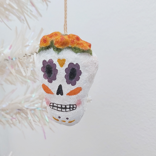 A spun cotton sugar skull ornament, hanging on a tree against a white background. Pic 1 of 5.