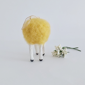 A back view of a yellow, vintage style spun needle felted spun cotton sheep ornament. White flowers sit next to her, against a white background. Pic 7 of 7. 
