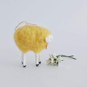 An opposite side view of a yellow, vintage style needle felted spun cotton sheep ornament. White flowers sit in front of her, against a white background. Pic 6 of 7. 