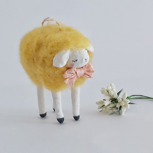 Another closer view of a yellow, vintage style needle felted spun cotton sheep ornament. White flowers sit next to her, against a white background. Pic 4 of 7. 