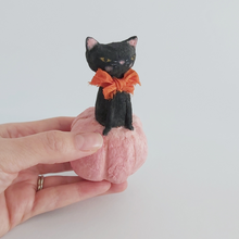 Load image into Gallery viewer, A vintage style, spun cotton black cat sitting in a pink pumpkin sitting in a hand against a white background. Pic 2 of 7. 
