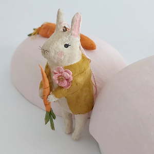 A close-up photo of a vintage style, spun cotton bunny ornament leaning against a light pink paper mache egg box. Pic 4 of 12. 