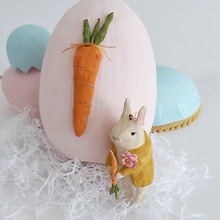 Load image into Gallery viewer, A vintage style, spun cotton bunny ornament leaning against a light pink paper mache egg adorned with a spun cotton carrot. Pastel eggs sit in the distance. Pic 12 of 12. 
