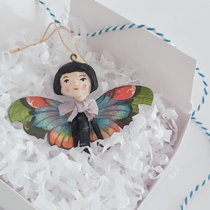 A vintage style spun cotton butterfly girl laying in a white gift box, on white tissue shredding. Pic 4 of 7. 