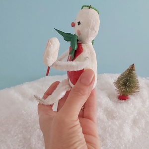 An opposite side view of a vintage style spun cotton candy man Christmas ornament, held in hand against a light blue background over fake snow. Pic 7 of 8. 