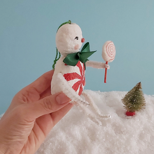 A side view of a vintage style spun cotton candy man Christmas ornament, held against a light blue background over fake snow. Pic 6 of 8. 