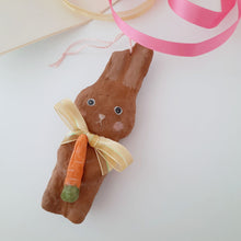 Load image into Gallery viewer, A chocolate brown, spun cotton bunny with a carrot and yellow bow laying on a white background.
