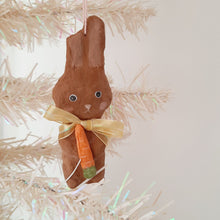 Load image into Gallery viewer, A spun cotton brown bunny ornament, with a carrot and yellow bow, hanging from a white tree, on a light background.
