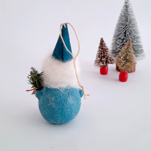 Load image into Gallery viewer, The back view of a gnome ornament, standing on a white surface with miniature Christmas trees in the background.
