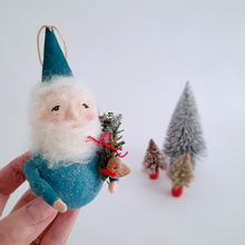 Load image into Gallery viewer, Hand holding a small gnome ornament with a blue hat and beard, surrounded by miniature trees on a light background.
