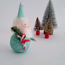 Load image into Gallery viewer, Side view of a mint green gnome  surrounded by small bottle brush trees on a light background.
