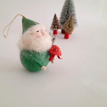 Load image into Gallery viewer, A spun cotton gnome ornament with a red mushroom on a white background; bottle brushes trees sit in the distance.
